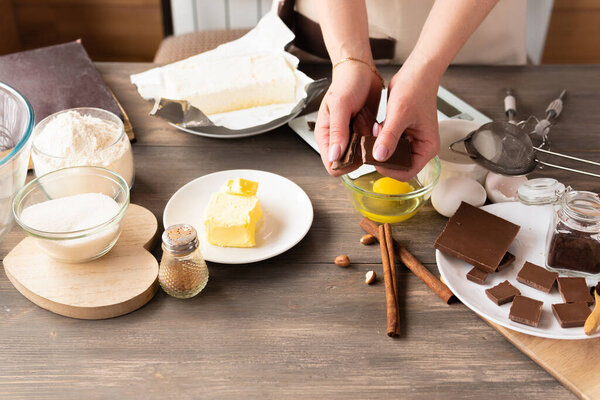 Ingredients for the dessert cupcake fondant and on a dark wooden background. Women's hands with chocolate.