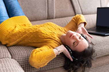 Kulaklıklı bir kız müzik dinliyor. Dizüstü bilgisayarı olan güzel bir kadın dairesinin penceresinin yanındaki kanepede oturuyor. O