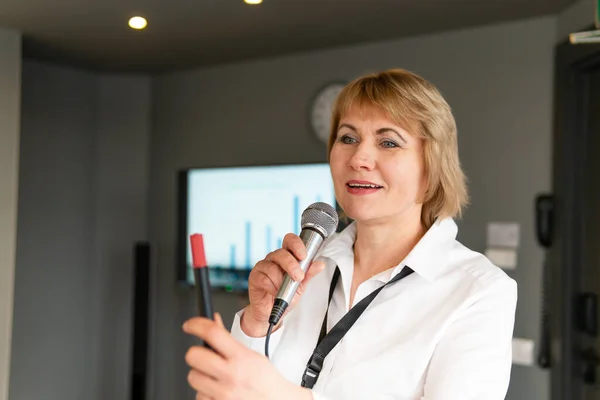 A business woman makes a presentation in a conference room with training. A middle-aged woman with a microphone performs
