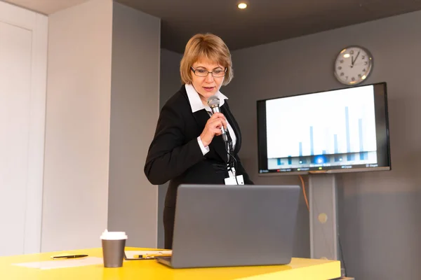 A business woman makes a presentation in a conference room with training. A middle-aged woman performs with a microphone.