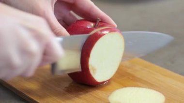 Mutfakta beyaz bir kız var. İnce yuvarlak dilimleri içine kırmızı elma kesme. Kız ahşap tahta üzerinde metal bir bıçak ile meyve keser. Bir elma üzerine damlama suyu. Yemek pişirme.