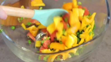 Kız ince doğranmış sebzeler yuvarlak, şeffaf, cam plaka karışımları: sarı biber, kırmızı domates, yeşil soğan. Salata ahşap bir spatula ile karıştırın. Mutfakta yemek.