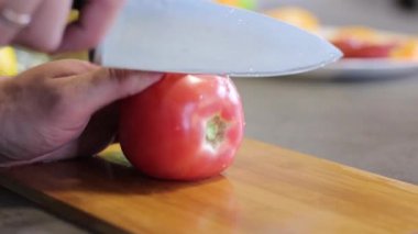 Mutfakta beyaz adam var. Kırmızı domates ince yuvarlak dilimleri içine kes. Adam ahşap tahta üzerinde metal bir bıçak ile sebze keser. Domates hamur ezmesi. Kesmeden sonra bıçağı erteleyin.