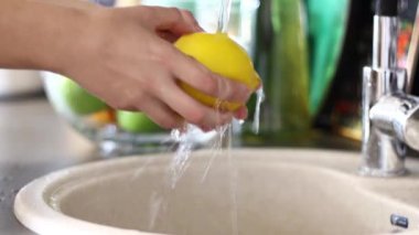 Meyve yıkayın. Su altında Lavabonun üstündeki kız sarı limon yıkar. Pişirmek için hazırlık. Yakınlarda yıkanabilir meyve içeren şeffaf bir plaka vardır.