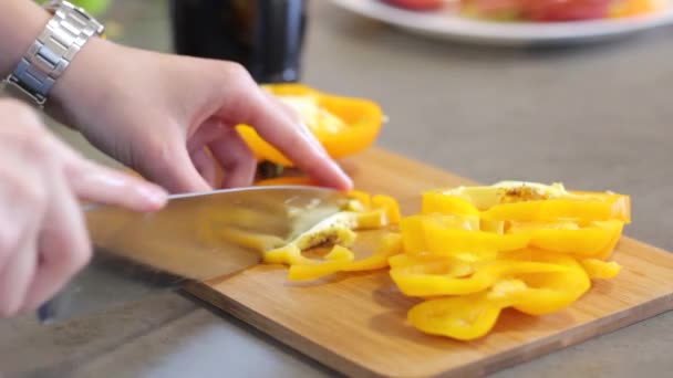 台所の白人の女の子黄色コショウの丸いスライスを細かく刻みます 女の子は木製の板の上に金属ナイフで野菜を切ります 料理をする 食品を粉砕 サラダの準備 クローズ アップ — ストック動画