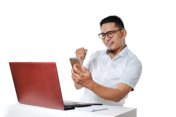 这位兴奋的亚洲年轻人坐在书桌上的笔记本电脑旁 成功地完成了在线自由职业者的工作 并获得了报酬 — 图库照片