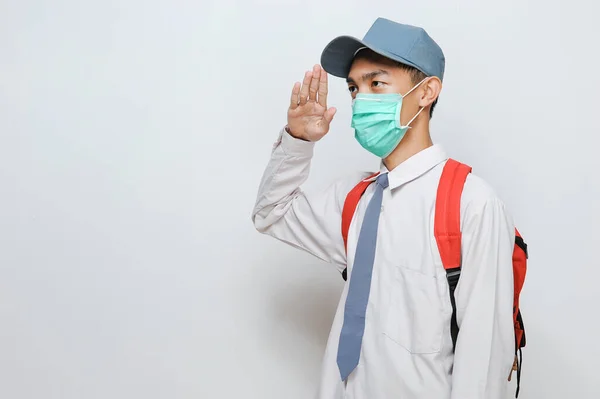 Indonesian Senior student of senior high school in Indonesian wearing protection face mask with school uniform giving salute, isolated on gray background