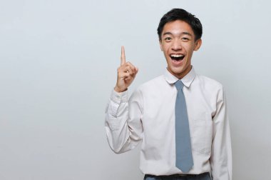 Endonezyalı öğrenci lise üniforması giyiyor ve başarılı bir jest yapıyor. Gri arka planda en iyi fikri buluyor.