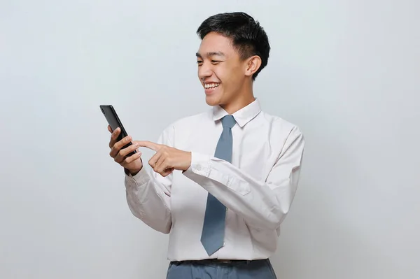 身穿高中制服的快乐印尼学生的画像 指着手机屏幕 与灰色背景隔离 — 图库照片