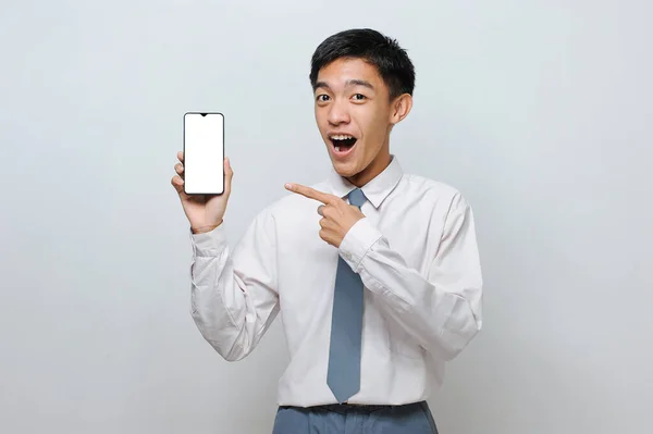 身着高中制服的印尼学生的画像 展示白色手机屏幕显示的东西 在灰色背景下被隔离 — 图库照片