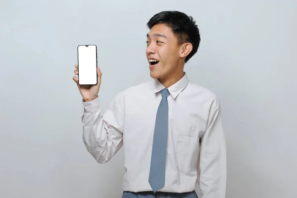 身穿高中制服的印尼学生在广告中展示白色的手机显示屏 这种显示屏在灰色背景下是孤立的 — 图库照片