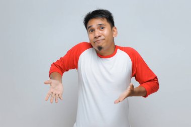 Kafası karışmış genç Asyalı adamın portresi. El ve omuzlarını kaldırırken şüpheleri var. Gri arka planda izole edilmiş.