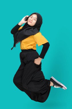 Mutlu Asyalı genç bir kızın gülümseyerek zıplarken ve telefonu kullanırken boy boy boy boy görüntüsü. Mutluluk, kaygısız ve pozitif konsept. Mavi arkaplanda izole