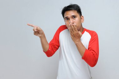 Gri arka planda izole edilmiş bir adam ağzını fotokopi alanını işaret ederek kapatıyor.