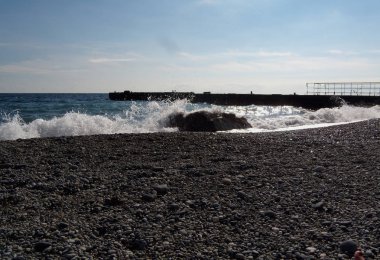 Dalgalar ve deniz sörfü ve deniz kıyısında taş sıçramaları. Sahilde taşlar ve kabuklar.