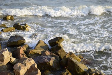 Sahilde deniz sörfü ve kayalar. Isleski taşlar ve dalgalar