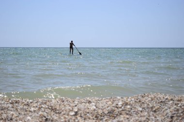 Kürek tahtası olan sörfçü dalgayı yakalıyor. Açık suda kürek yatılı.