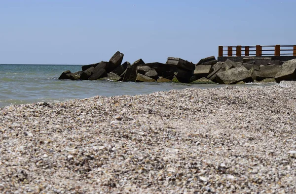 Пірс і каміння. Морський пірс з пірсом, обладнаний дерев'яними поручнями. Блакитне небо і море — стокове фото