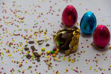 Renkli bulanık konfeti ve diğer renkli yumurta ile beyaz arka plan içinde renkli çikolata ile Kırık altın çikolata paskalya yumurtaları