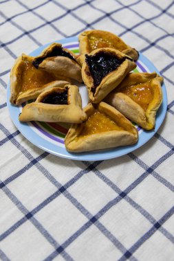Hamantash Purim Yaban Mersini ve kayısı reçeli kurabiye mavi kareler arka plan ile masa örtüsü üzerinde renkli plaka üzerinde