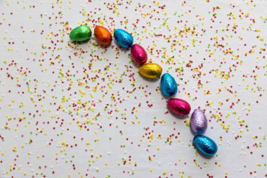 Beyaz arka plan ve renkli konfeti birçok hizalanmış renkli çikolata paskalya yumurtaları