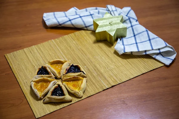 Hamantash Purim biscoitos de mirtilo e geléia de damasco com fundo de mesa de madeira e vela em forma de estrela David — Fotografia de Stock