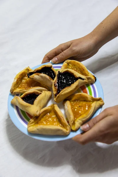 Kvinna händer håller en färgad platta med Hamantash Purim Blueber — Stockfoto