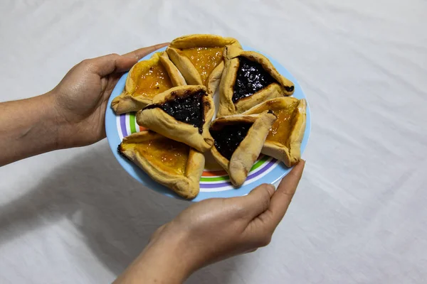 Kadın elleri Hamantash Purim Blueber ile renkli bir tabak tutuyor.