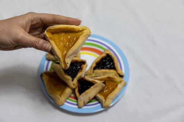 Mulher mão segurando biscoito hamantash em cima da sagacidade placa colorida — Fotografia de Stock