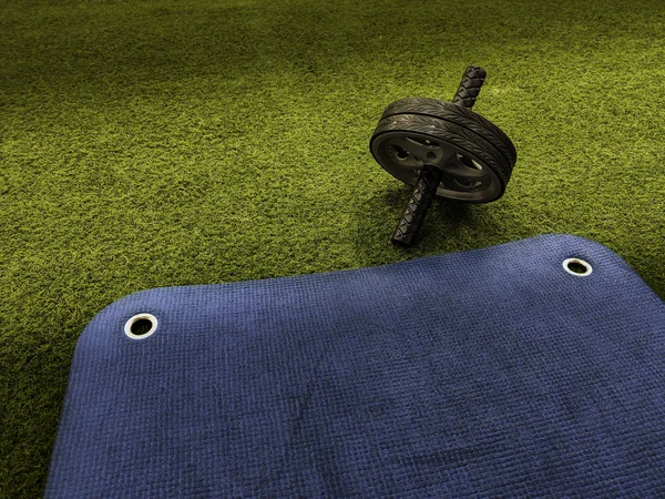 Abs wheel on green artificial grass and blue training mat — Stockfoto