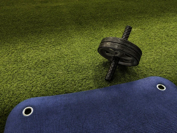 Abs wheel on green artificial grass and blue training mat — Stock fotografie