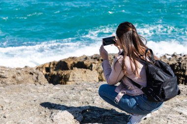 Çömelmiş, akıllı telefonuyla sahilin fotoğraflarını çeken bir kadın.