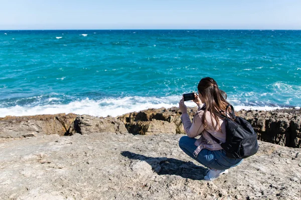 Çömelmiş, akıllı telefonuyla sahilin fotoğraflarını çeken bir kadın.