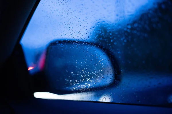 Car right rear mirror view from inside the car with drops on the window