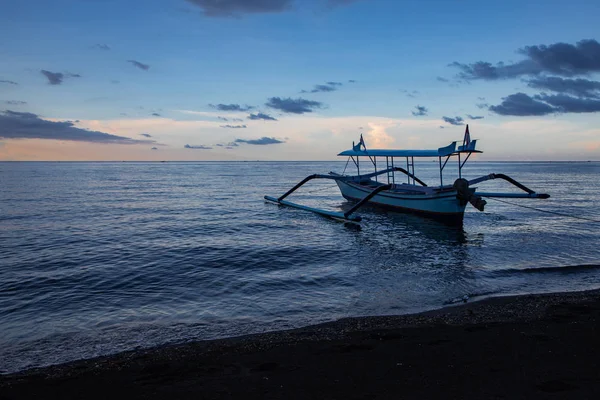Blue hour over calm ocean and black sand beach with balinese boa