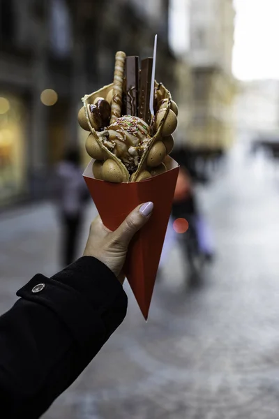 stock image Woman hand holding a bubble waffle with ice cream and candies on