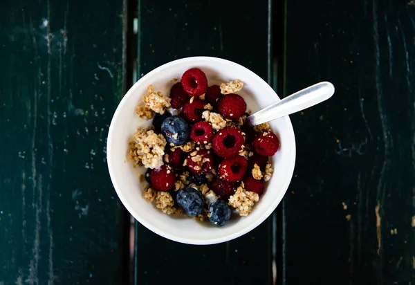 Мюслі, дикі ягоди та йогурт сніданок на верхній частині миски з чорним дерев'яним фоном — стокове фото