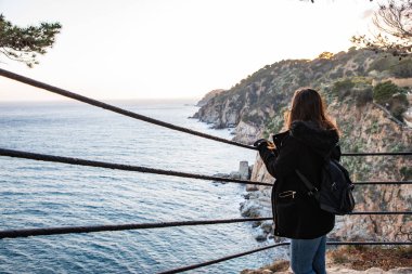 Kayalık kayalık kıyı şeridinde gün batımına bakan kadın