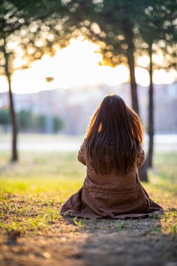 Sonbahar gün batımı sırasında bir parkta çim üzerinde oturan güzel kadın