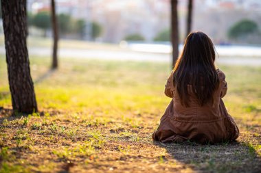 Sonbahar gün batımı sırasında bir parkta çim üzerinde oturan güzel kadın