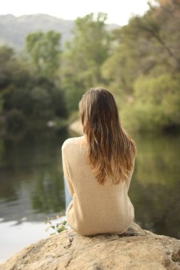 Göl yakınındaki bir kayaya oturan kadın