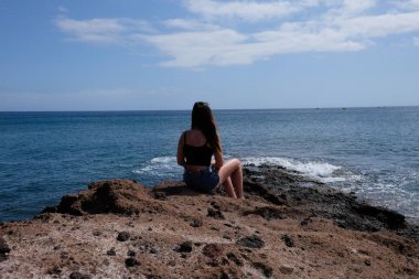 Denizde görünümlü volkanik kayaların üzerinde oturan kız