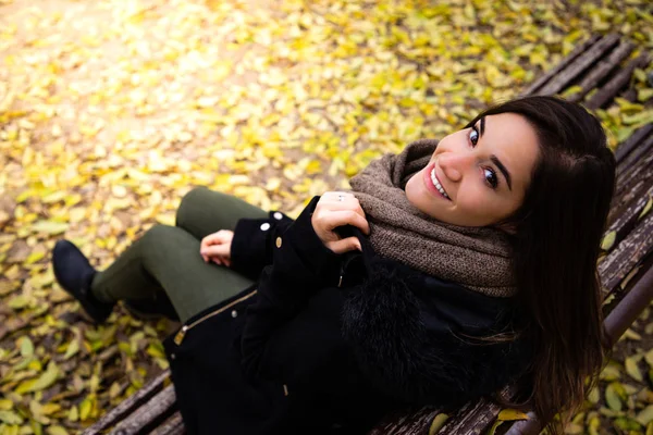 Beautiful woman sitting on a bench surrounded by yellow fall leaves top shot — Stock Photo, Image