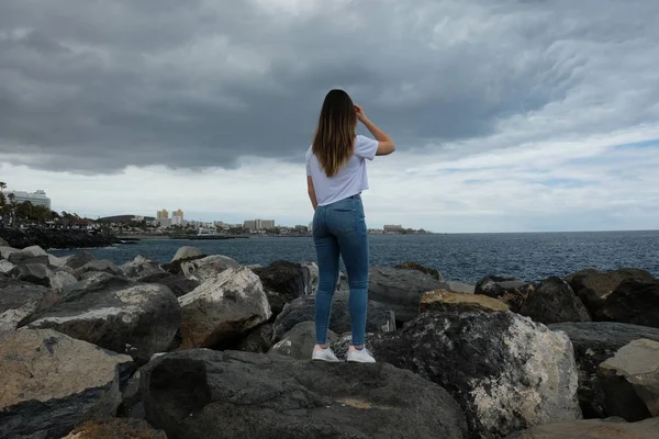 Menina bonita de pé em rochas de praia olhando para o mar — Fotografia de Stock