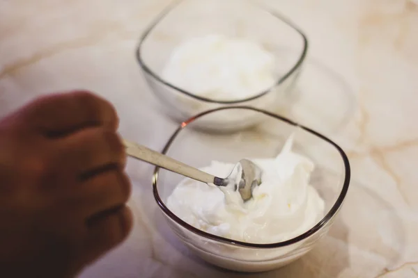 Mão colocando creme em tigela transparente — Fotografia de Stock