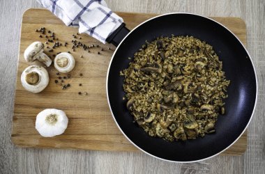 Sarımsak, biber ve mantar ile süslenmiş bir ahşap kesme tahtasında mantar risotto ile Pan