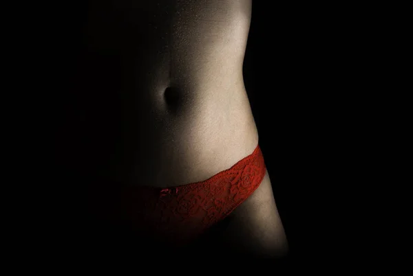 Barriga de mulher bem formada com calcinha vermelha erótica no fundo preto baixo tiro chave — Fotografia de Stock
