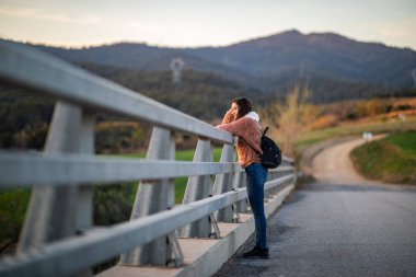 Gün batımı sırasında metal bir çit üzerinde eğilirken güzel bir kadının yan çekim