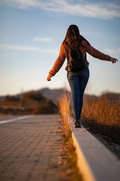 Beautiful woman walking and balancing on street curb or curbstone during sunset — Stock Photo, Image