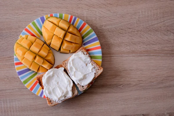 Tostadas de queso con mango cortado en cubos en un plato colorido sobre una mesa de madera — Foto de Stock